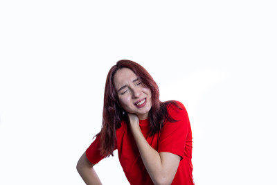 身穿红色衬衫的白人女性因疼痛而捂着脖子，脸上露出痛苦的表情