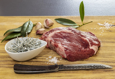 一块生牛肉，蒜瓣，月桂叶，刀和铁钉放在木头上