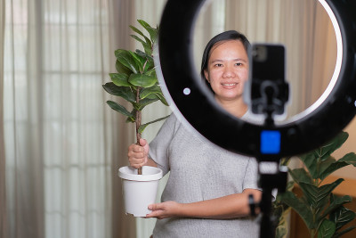 亚洲女性用智能手机在线直播，在家里卖人造植物