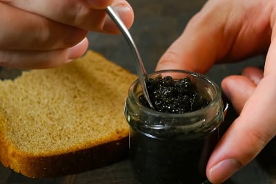 用勺子在玻璃罐中搅拌黑鱼子酱。