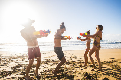 Group of friends play at the beach with water guns