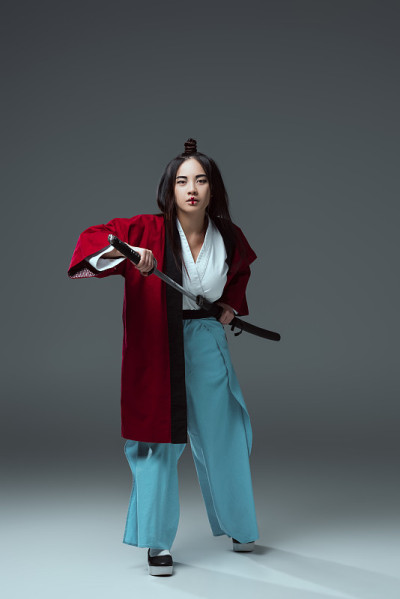 全长度的观点，年轻的亚洲妇女在和服持有武士刀和看在灰色的相机