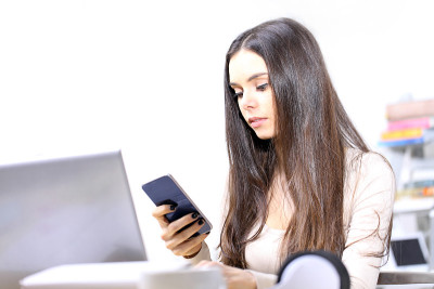 一个年轻女子在办公桌旁用手机发短信