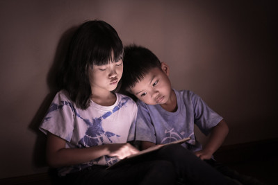 兄弟姐妹一起在昏暗的灯光下看平板电脑屏幕。