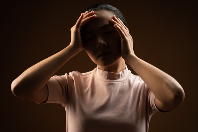 亚洲妇女生病头痛孤立站在米色背景。低调。