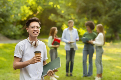 校园生活。在校园里用笔记本和咖啡摆姿势的亚洲学生