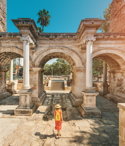 快乐的女游客旅行者发现有趣的地方和受欢迎的景点和漫步在安塔利亚老城，土耳其。罗马著名的哈德良大门