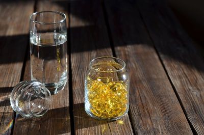 装有维生素的黄色凝胶胶囊玻璃罐和一杯水。