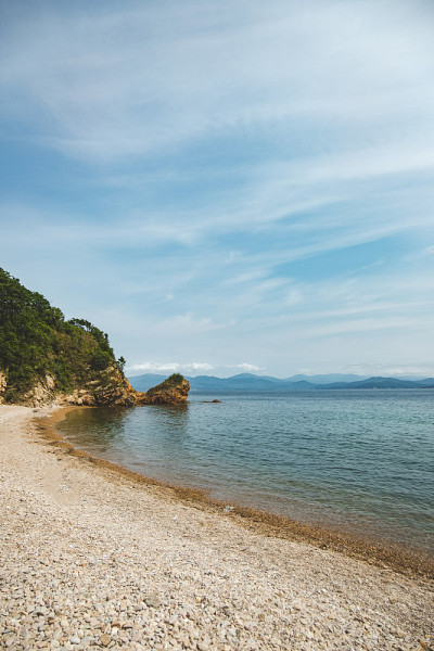 夏日蔚蓝清澈的大海全景。浅浅的透明的海洋，周围有珊瑚礁、岩石和绿色的小山。日本海洋。俄罗斯的滨海边疆