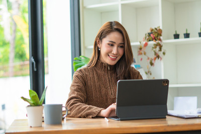 微笑美丽的年轻亚洲女人工作在笔记本电脑