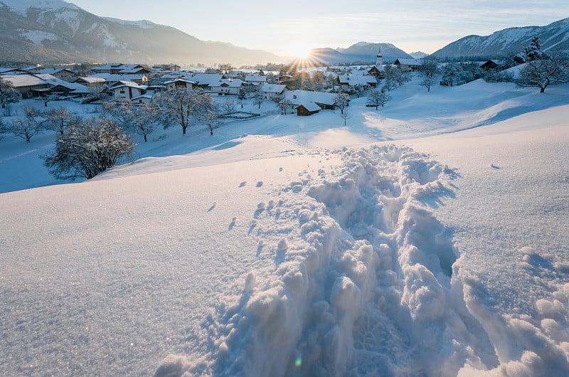 在奥地利泰洛尔的维尔德米明的高山村庄里，厚厚的雪道穿过冬日的夕阳景观