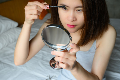 年轻的亚洲妇女用睫毛棒涂黑睫毛膏的肖像。