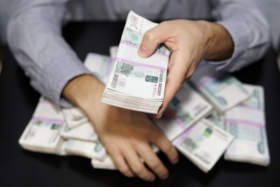 男人的手伸向一叠钱。一百万卢布放在黑色的桌子上。财富的概念，成功，贪婪和腐败，对金钱的欲望