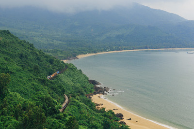 越南岘港海凡山口顺化的琅哥海滩全景。火车在海边的铁路上行驶，绿色的森林，美丽的自然景观，海浪