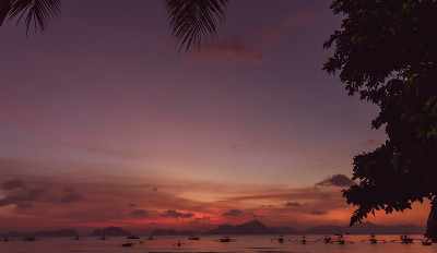 热带海滩上美丽的日落。鸟瞰图的戏剧性的夜空和船的剪影。风景如画的巴拉望岛，菲律宾。傍晚热带海景。夏季