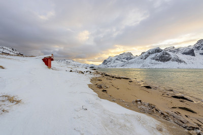 挪威的罗浮敦群岛和它们美丽的日落冬季风景。白雪皑皑的海滩上红色的房子，一派田园风光。北极圈的旅游胜地