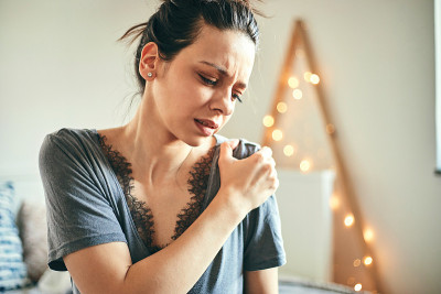 坐在床上时肩膀疼痛的妇女。