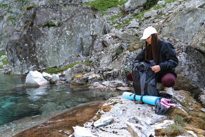 女孩旅行者在白色的帽子和黑色的夹克坐在附近的山湖和打开背包