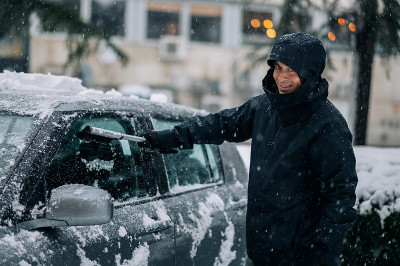 中年男子正在清理汽车上的冰雪