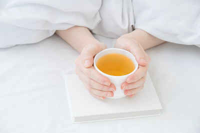 女性的手从毯子下拿着一杯白色的绿茶在她们的手中