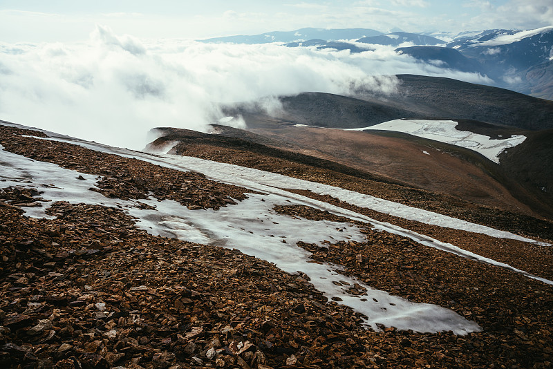 风景优美的高山景观与层峦叠嶂的地平线在密集的低云层。在高地的云朵中，美妙的层层叠叠的山形浮雕。雪山和