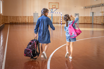 空空的学校体育馆里背着书包的小女孩们。