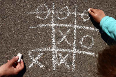 一个孩子和他的妈妈在柏油路上用粉笔玩井字游戏