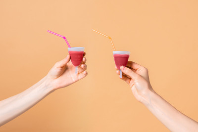 经期杯环保可重复使用，硅胶在女性手中孤立在橙色背景与鸡尾酒管