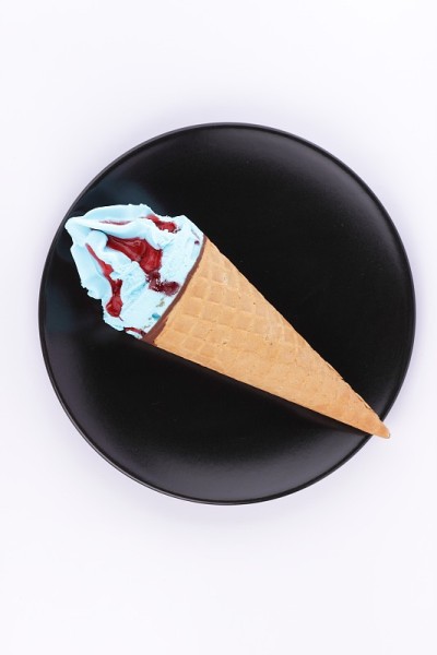 冰淇淋装在一个华夫饼杯里，里面有五颜六色的馅和红色的果酱，放在一个黑色的盘子里，还有一个专门为设计师