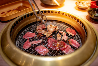 厨房用钳子在金色的炉子里烤着牛肉和培根。在餐厅享用韩国烧烤自助餐。
