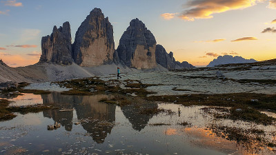 在意大利Dolomites的Drei Zinnen山脉上，一位妇女正在欣赏日落。山峰倒映在船桨上。群