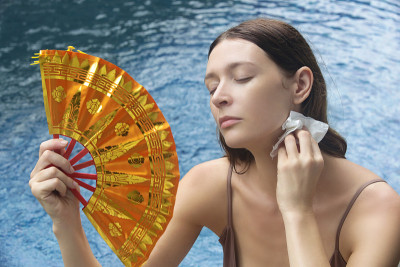 一名女子用扇子对抗热浪。在一个炎热的夏天，一个年轻女子在水边的肖像。