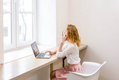 一个女人在办公室一边用笔记本电脑一边打电话。女商人在和客户通电话。女性创业、职业、网购的概念。商务女