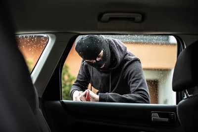 戴着巴拉克拉瓦盔式帽的偷车贼试图撬开一辆车
