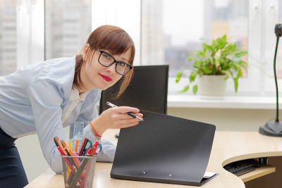 一位戴眼镜的漂亮女商人，在办公室靠窗的工作桌旁签署文件