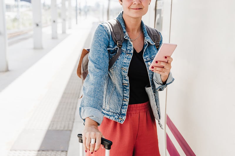 一个白人背包女在火车站拿着行李准备赶火车。拿着手机使用app。旅游概念