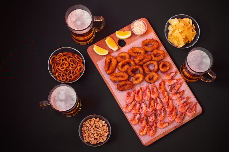 大杯啤酒和啤酒小吃在天黑。前视图。