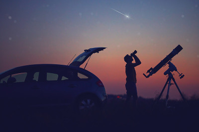 一个人的剪影，汽车，望远镜和乡村星空下。