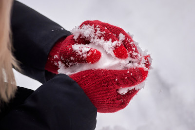 双手戴着红色手套，在雪的背景上做一个雪球。冬季娱乐活动