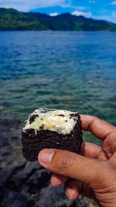 有人在清澈的海边享受美味的布朗尼蛋糕