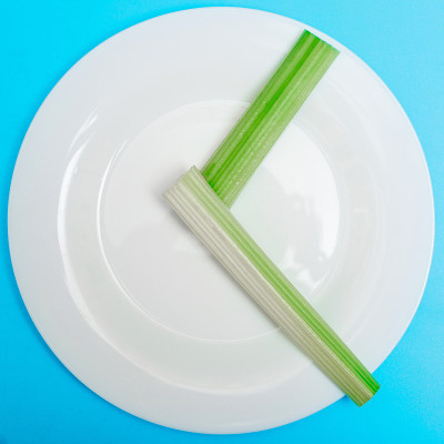 间歇性禁食，饮食概念。一个空盘子作为一个表盘和豆荚的卖家作为一个时钟指针在蓝色的背景。