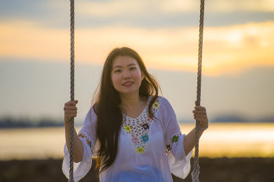 年轻美丽和快乐的亚洲日本女人享受暑假旅行在海滩度假胜地微笑愉快的秋千有乐趣，感觉自由和放松的在海上的