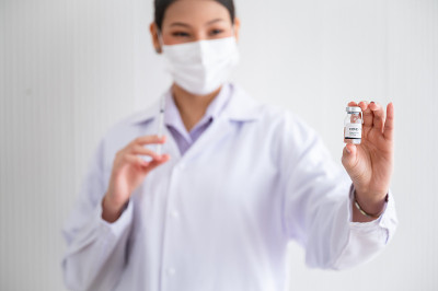 女医生戴着口罩，拿着装有疫苗的注射器。实验室里的冠状病毒19。防范COVID-19病毒的概念。