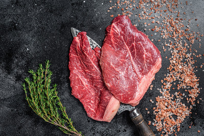 屠夫选择牛肉生牛排在屠刀上。黑色背景。俯视图