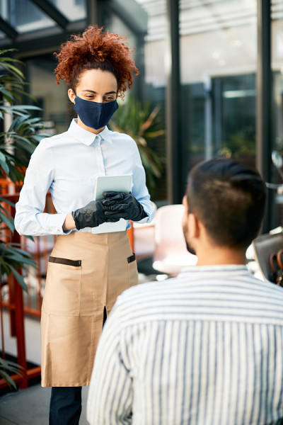 快乐的女服务员戴着口罩在咖啡馆为顾客点菜。