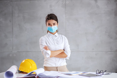 年轻的女建筑师戴着面罩，双手交叉站在冠状病毒。虽然这是日冕爆发架构师必须工作。