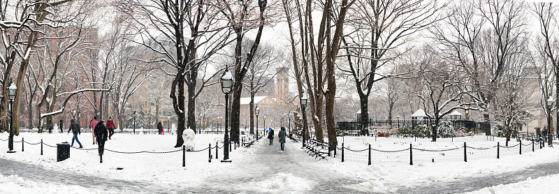 在纽约，人们在冰雪覆盖的华盛顿广场公园中行走的全景冬季场景