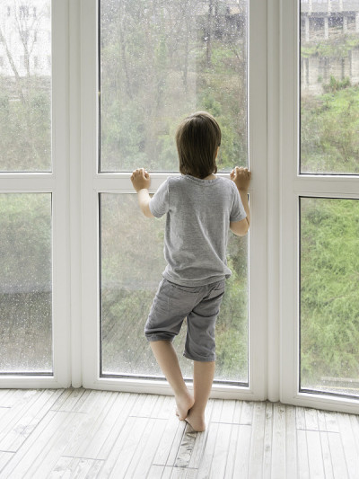 小男孩透过布满雨滴的潮湿全景窗户望向户外。冠状病毒COVID19隔离。多雨的夏天的天气。孩子一个人呆