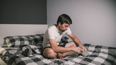 年轻白人男子在家测量血压，坐在床上在家测衣服。男性用医疗仪器血压计测量自己的血压。年轻时患高血压。