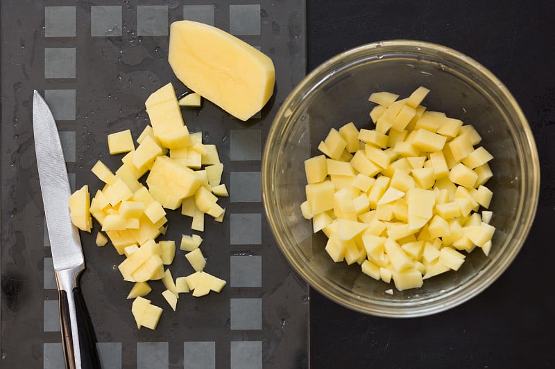 Top view of cut raw potato in glass bowl and knife